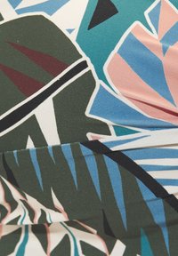 Primer plano de tela con patrones abstractos de hojas tropicales en verde, azul, rosa, negro y blanco, con pliegues visibles.