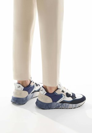 Baskets de sport bleu et crème avec un design en matériaux mixtes, lacets blancs et semelle texturée avec le logo "Niche" au talon.