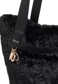 Borsa tote in ecopelliccia nera con superficie testurizzata, manici in pelle nera e logo in tonalità oro. Arricchita da accessori portachiavi in metallo.