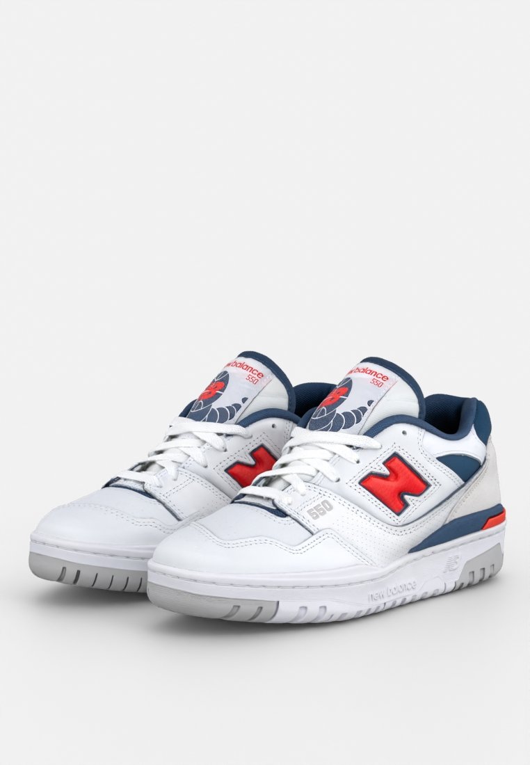 Sneaker bianche con accenti blu e rossi. Presentano pelle texturizzata, linguetta imbottita e suole in gomma. Logo "New Balance" e numero di modello visibili.