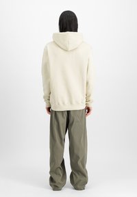 Gräddfärgad hoodie med en bakseam och huva, tillsammans med löst sittande olivgröna byxor. Mjuk tyg utan synliga mönster eller detaljer.