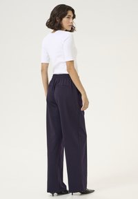 Haut blanc à manches courtes associé à un pantalon large violet foncé avec une taille élastique et deux poches arrière.