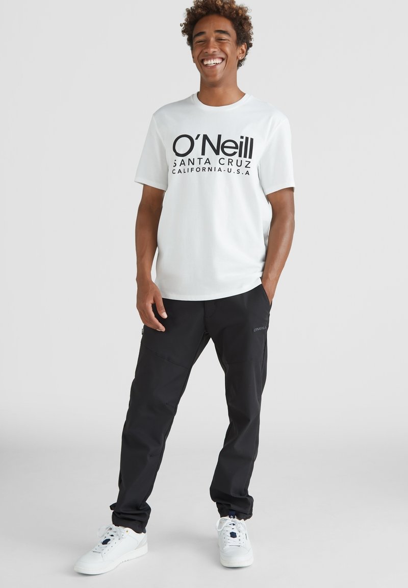 Camiseta blanca de manga corta con texto negro que dice "O'Neill Santa Cruz California, U.S.A.", combinada con pantalones cargo negros y zapatillas blancas.