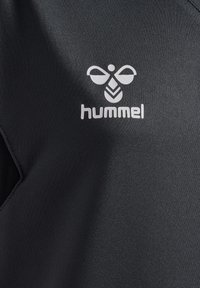 Schwarzes Sportshirt mit glatter Textur und kurzen Ärmeln, ausgestattet mit einem weißen "hummel"-Logo und einem stilisierten Bienenmotiv auf der Vorderseite.