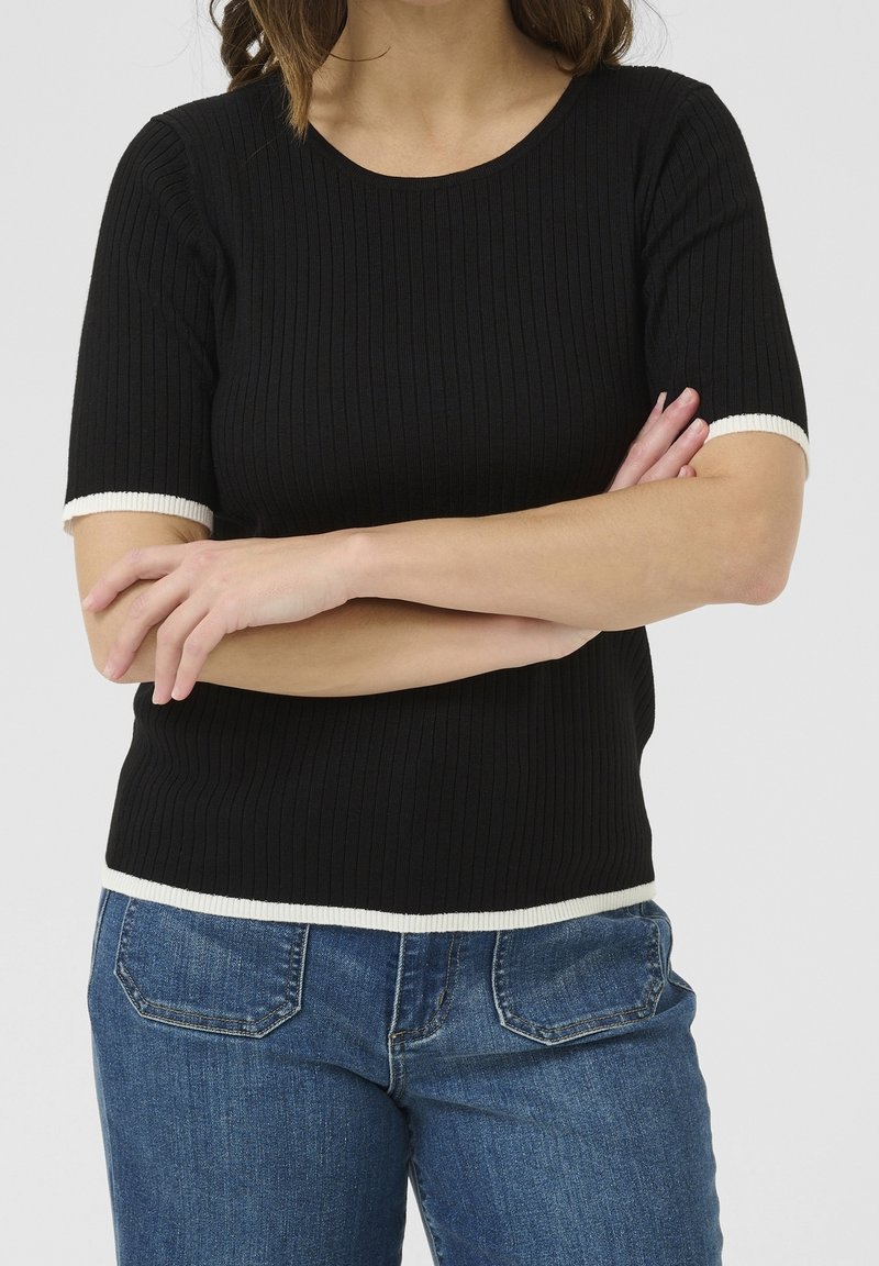 Top negro de manga corta con textura acanalada y mangas y dobladillo con ribete blanco, diseño ajustado, combinado con jeans de mezclilla de lavado medio.