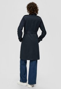 Granatowy płaszcz trench z paskiem w talii, długimi rękawami i kieszeniami. Wykonany z gładkiego materiału, z tylnym rozporkiem i usztywnionym kołnierzem.