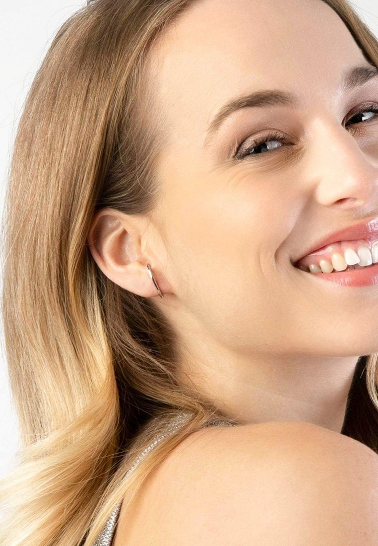 Zilveren hoepel oorbellen, cirkelvormig ontwerp, gepolijste afwerking, minimalistische stijl, gedragen door een lichtgekleurde persoon met golvend blond haar.