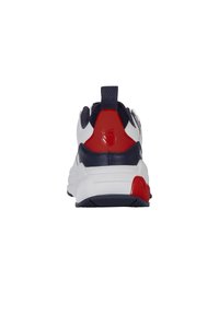 Fehér és sötétkék sneaker piros kiegészítőkkel, texturált hátsó résszel, robusztus talppal és logós részlettel. Párnázott nyak és fűzős kialakítás.