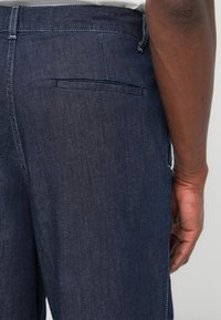 Σκούρο τζιν παντελόνι με πίσω τσέπη, ίσια γραμμή και διακριτικές ραφές. Λείο ύφασμα με κλασικό σχέδιο.