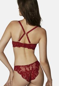 Soutien-gorge en dentelle rouge et string assorti, ornés d'un motif floral, de bords festonnés et de bretelles réglables avec des accents dorés. Texture transparente.