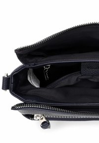 Granatowa skórzana torba w środku z dwoma przegródkami, zamkiem błyskawicznym oraz gładką podszewką. Posiada małą metkę i widoczne detale szycia.