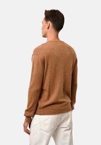 Brauner Cashmere-Pullover mit langen Ärmeln, Rundhalsausschnitt und gerippten Bündchen. Glatte Textur mit lockerer Passform, kombiniert mit weißen Hosen.