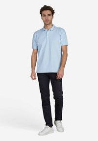 Lichtblauwe polo met een twee-knopen knoopsluiting, korte mouwen en een contrasterende kraag. Gecombineerd met donkere slim-fit jeans en witte sneakers.