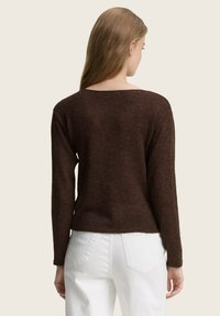 Sweater en tricot brun à manches longues et décolleté large, associé à un jean blanc taille haute, vu de dos.