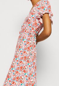 Abito floreale con sfondo rosa, decorato con fiori rossi e blu, maniche corte a volant e vita cintrata con un nastro.