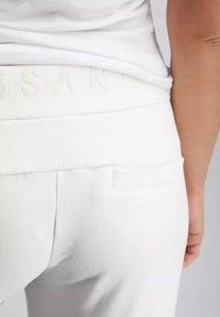 Weiße Baumwoll-Jogginghosen mit einem strukturierten Bund, ausgestattet mit einem dezenten geprägten Logo und einer einzelnen Gesäßtasche.
