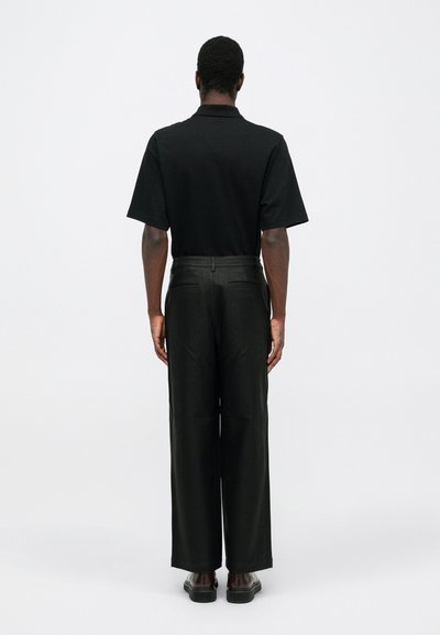 Black short-sleeve polo shirt paired with dark, wide-leg trousers. The outfit features a clean design with minimal detailing.
