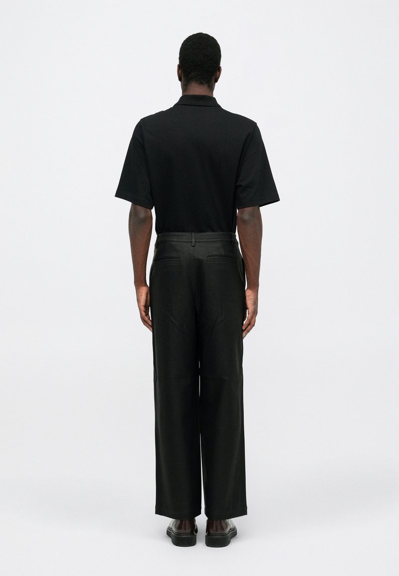 Schwarzes Poloshirt mit kurzen Ärmeln kombiniert mit dunklen, weiten Hosen. Das Outfit zeichnet sich durch ein klares Design mit minimalen Details aus.
