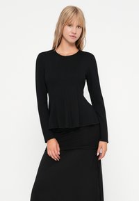 Schwarzes Langarm-Oberteil mit tailliertem Oberteil und gefaltetem Saum. Glatte Textur und runder Ausschnitt, kombiniert mit einem schwarzen Rock.