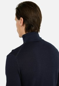 Maglione a collo alto lavorato a maglia di colore blu navy con un design aderente, colletto a coste e spalle senza cuciture, che mette in mostra una texture liscia.