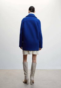 Blauwe oversized wollen blend jas met een gestructureerde kraag, een getextureerde gebreide trui, een korte witte zoom en beige kniehoge hakken.