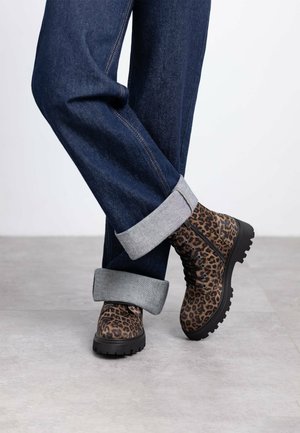 Botas de tobillo con estampado de leopardo, hechas de un tejido texturizado con suelas de goma negras, combinadas con pantalones de mezclilla oscuros arremangados con puños grises.