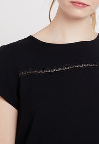 T-shirt nera con maniche corte, caratterizzata da un dettaglio in pizzo testurizzato sul petto e un collo rotondo. Tessuto morbido.