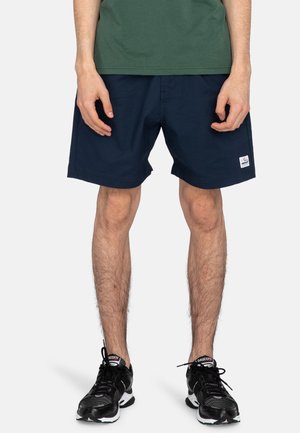 Navy blue swim shorts with a fabric texture, featuring an elastic waistband and a small white logo patch on the lower left side.