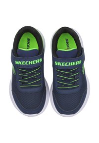 Zapatillas de color azul marino con material de malla, acentos verdes, suela blanca, cordones elásticos y una correa de velcro con la marca "SKECHERS".