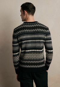 Sweter dziany z czarno-kremowo-szarym geometrycznym wzorem, okrągłym dekoltem oraz ściągaczami przy mankietach i dolnej części. Teksturowany materiał z mieszanki wełny.