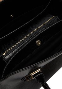 Intérieur d'un sac à main en cuir gaufré serpent noir avec une poche zippée et des accastillages dorés. Comprend un doux doublage en textile et plusieurs compartiments.