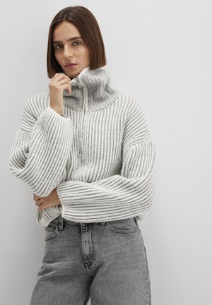 Grau gestreifter, gestrickter Pullover mit hohem Kragen und halbem Reißverschluss. Verfügt über breite, verkürzte Ärmel und eine lockere Passform. Kombiniert mit grauen Jeans.