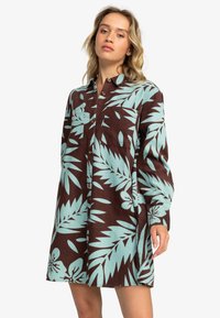 Brown long-sleeve dress featuring a turquoise leaf pattern, button front, and two chest pockets; made from textured fabric.
