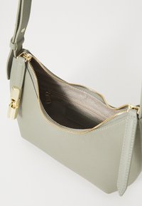 Borsa a tracolla verde in pelle con una texture liscia, cerniera e accessori dorati. Design compatto con un ampio interno e una tasca con zip.