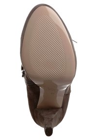 Zapato de tacón alto de ante marrón con punta afilada, que presenta una suela suave y brillante con un agarre texturizado y un detalle de cremallera en el lateral.