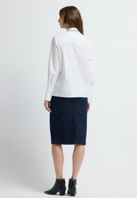 Witte blouse met lange mouwen, gecombineerd met een knie-lange marineblauwe rok met een textuurpatroon, en zwarte enkellaarsjes.
