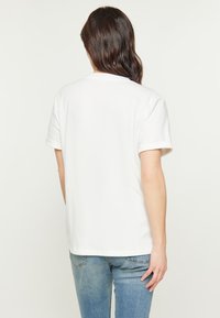 Hvid kortærmet T-shirt lavet af bomuld, med rund halsudskæring og afslappet pasform. Stoffet har en glat tekstur med opsmøgede ærmer.