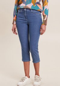 Pantalons capri en denim bleu avec une coupe slim, dotés d'un design à cinq poches et de ourlets. Associés à des baskets blanches.