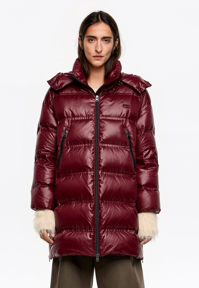 Bordowy puchowy płaszcz z błyszczącym wykończeniem, wyposażony w zamek błyskawiczny, dwie zapinane na zamek boczne kieszenie oraz futrzane akcenty na rękawach.
