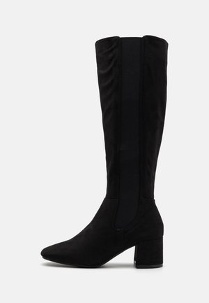 Black suede knee-high boots with a pointed toe and a chunky heel. Side elastic panels for comfort and fit. Smooth texture.