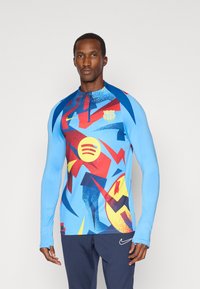 Bluza sportowa z długim rękawem w jasnoniebieskim kolorze, z abstrakcyjnymi wzorami w kolorze czerwonym, żółtym i niebieskim. Posiada zamek błyskawiczny na ćwierć długości oraz akcenty logo.