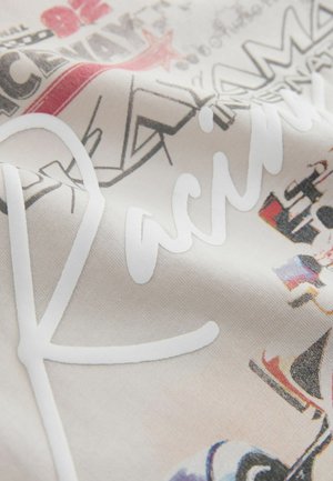 Puuvillakangas, jossa on teksturoidulla pinnalla valkoinen kursivoitu "R" ja värikkäitä graafisia kuvioita eri sävyissä vaaleaa taustaa vasten.