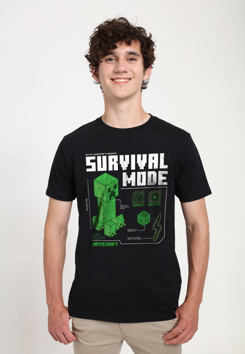 Mladý muž se usmívá, má na sobě černé tričko Minecraft s pixelovým motivem zeleného Creepera a nápisem "Survival Mode" na bílém pozadí.