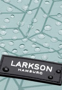 Tissu imperméable vert menthe avec un motif géométrique, ornée de gouttelettes en relief. Étiquette noire avec "LARKSON HAMBURG" en texte blanc.