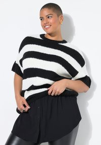 Pull en tricot surdimensionné à rayures noires et blanches avec des manches courtes, associé à une chemise noire à boutons et des leggings noirs. Tissu texturé.