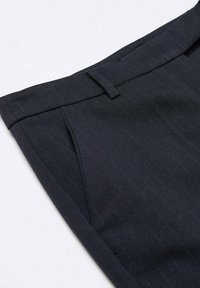 Pantalons noirs à rayures avec un devant plat, passants de ceinture et poches latérales. Fabriqués dans un tissu texturé, avec une coupe ajustée.