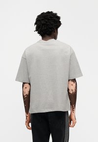 Γκρι βαμβακερό μπλουζάκι με κοντά μανίκια, άνετη εφαρμογή και λαιμόκοψη τύπου crew. Το ύφασμα φαίνεται ελαφρύ και απαλό. Πλάτη μοντέλου σε προβολή.