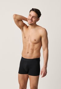 Schwarze Boxershorts mit elastischem Bund, glatt am Bauch und den Oberschenkeln anliegend, aus weichem, dehnbarem Stoff.