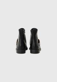 Botas de tornozelo em couro preto com acabamento liso, fecho de zíper na parte de trás e detalhe dourado na lateral. Solas robustas e design minimalista.