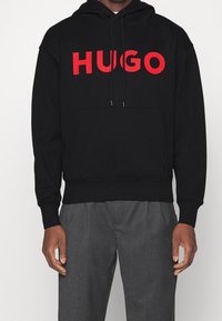 Svart huvtröja med stort rött "HUGO"-tryck, känguruficka, justerbara dragsnören och ribbade muddar och nederdel.
